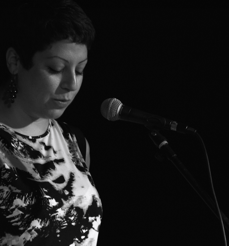 Image of Justine reading into the microphone, black and white with black background